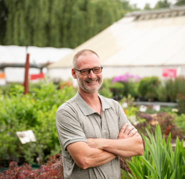 Man smiling with arms crossed in garden center at Studley Flower Gardens NH by Studley Flower Gardens