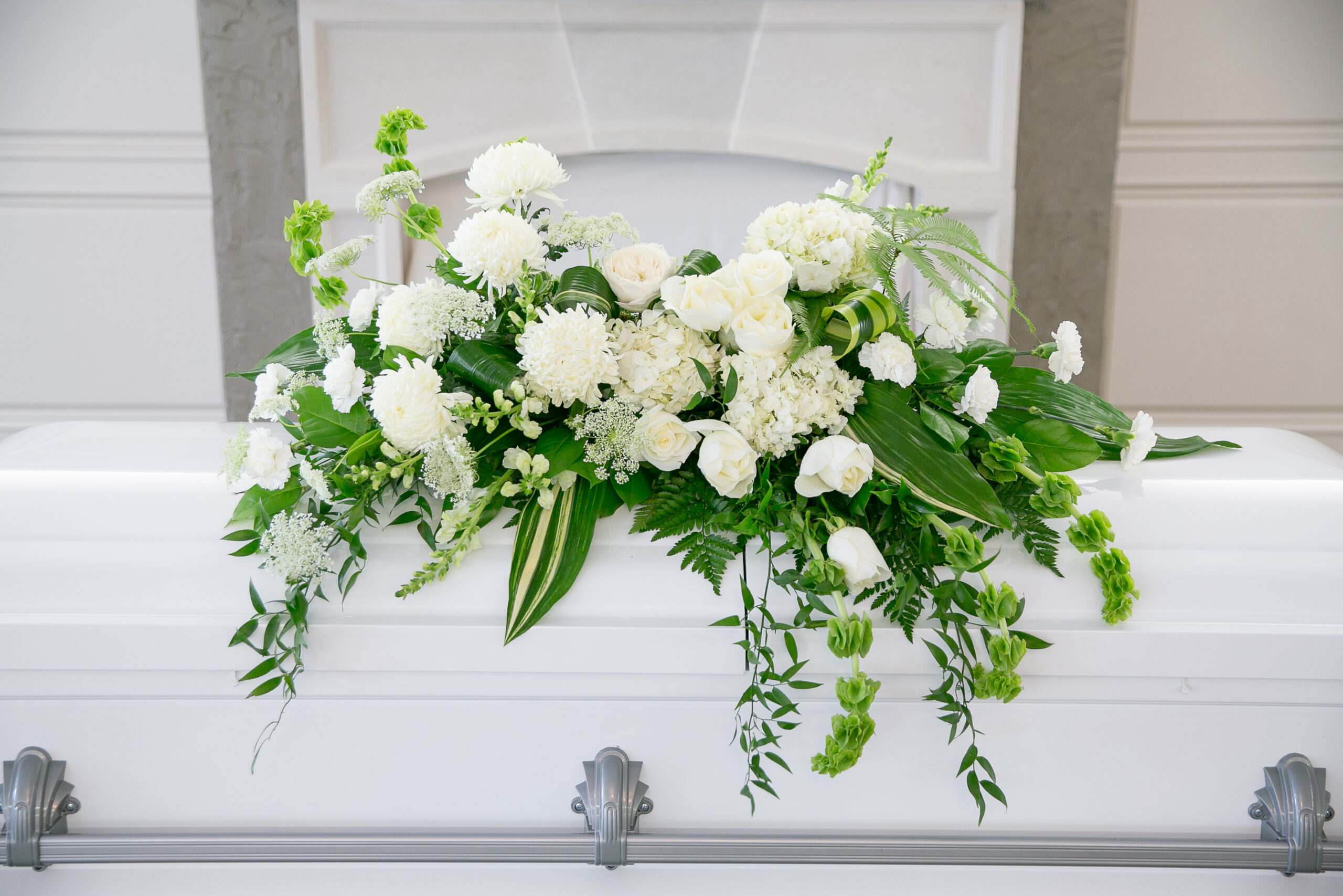 Dignity casket spray with white blooms and greenery by Studley Flower Gardens