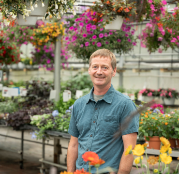 Man standing in greenhouse with colorful hanging flowers at garden center by Studley Flower Gardens