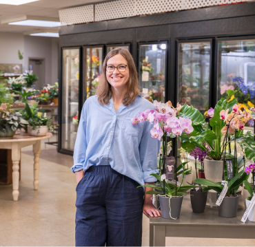 Woman standing by orchids and plants inside garden center by Studley Flower Gardens