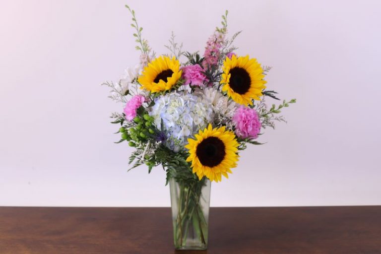 Sunlit Cheer Bouquet with pastel blooms and sunflowers in glass vase by Studley Flower Gardens