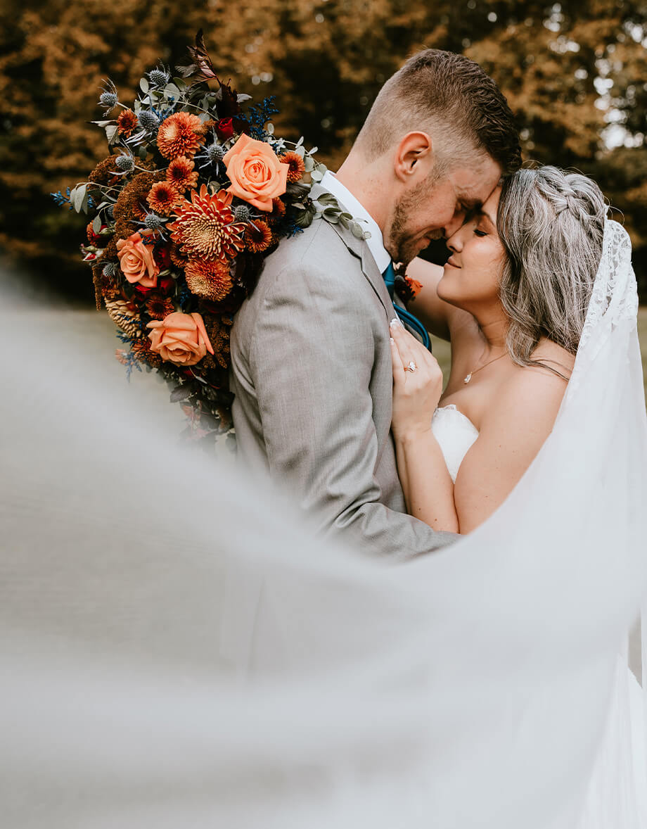 Bride and groom embracing with bouquet of orange and red flowers by Studley Flower Gardens